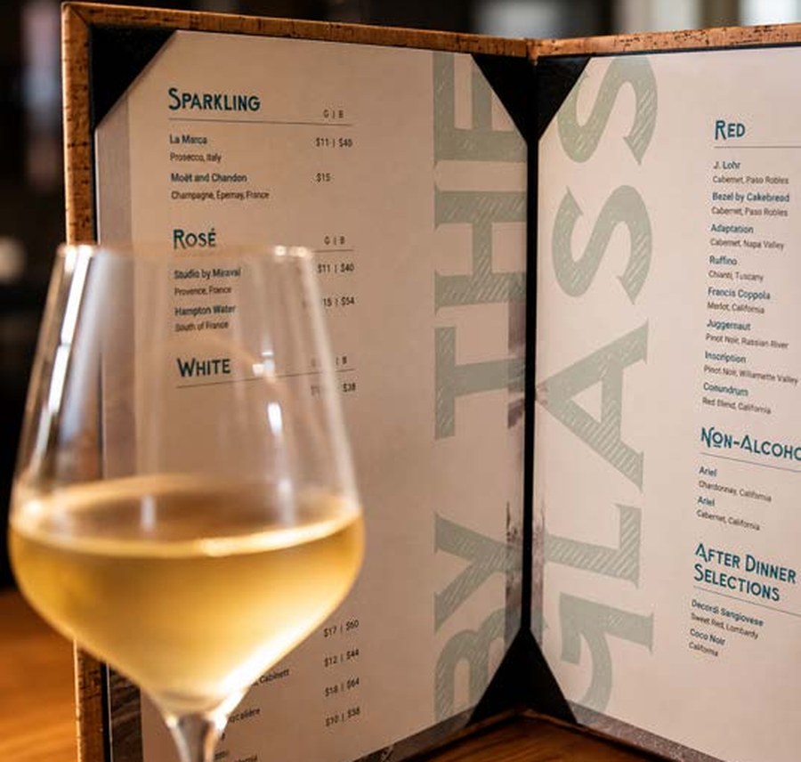 Glass of white wine beside the Tradewinds 41 wines-by-the-glass list